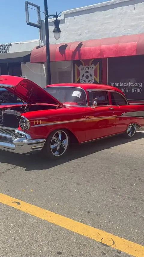 A shiny, red classic car with its hood propped open on display at an outdoor car show.